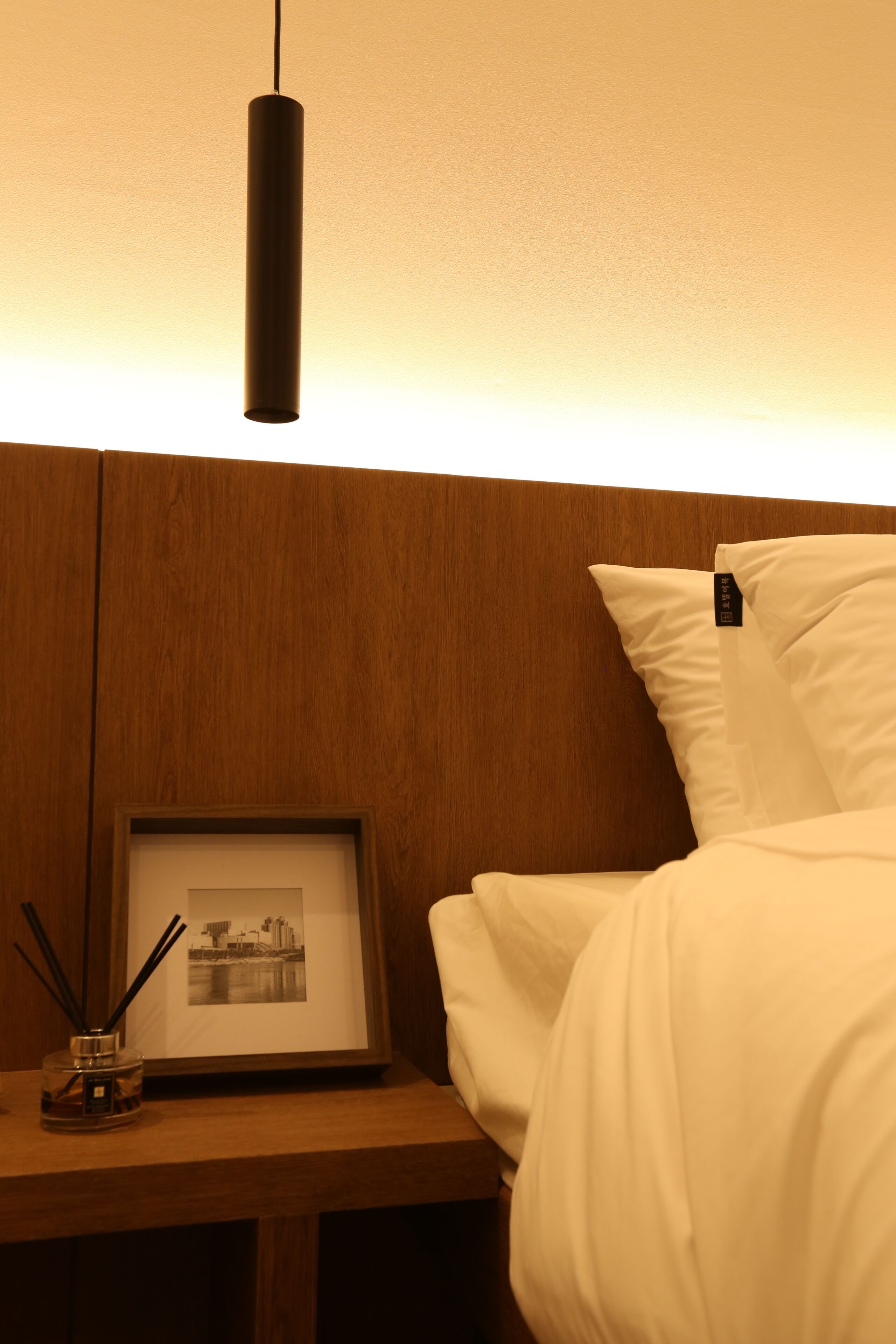 A neatly made bed with white bedding, a framed picture on the nightstand, and a hanging light fixture.