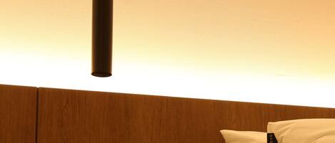 A neatly made bed with white bedding, a framed picture on the nightstand, and a hanging light fixture.