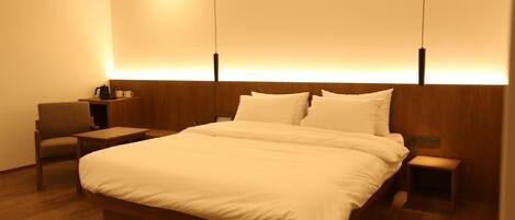 Ein modernes Hotelzimmer mit einem Holzbett, einem kleinen Nachttisch, einem Stuhl und einem Beistelltisch.