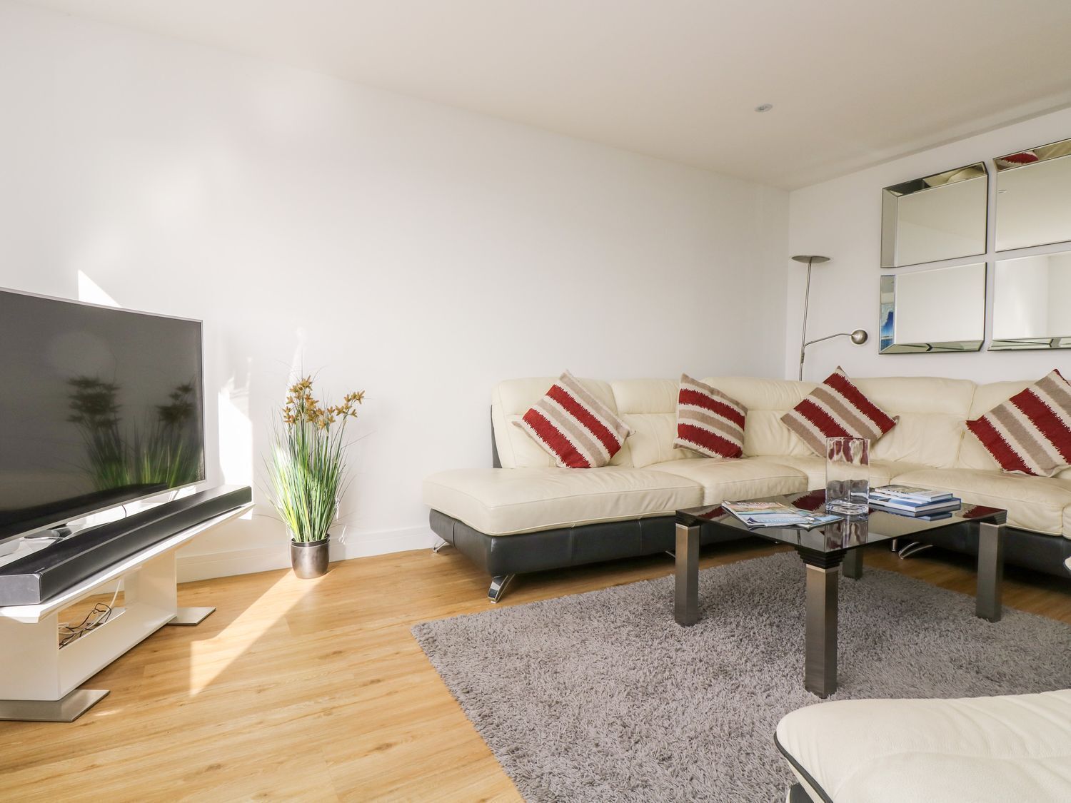 Una sala de estar moderna con un televisor de pantalla plana, un sofá color beige con almohadones a rayas, una mesa de centro y una alfombra gris.