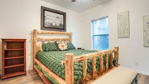 A rustic wooden bed with a green quilt, a wooden nightstand, a framed picture on the wall, and a window with a view of trees. - Private Lake Access, Enjoy Serenity @ Bunk South (Palm City)