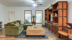 A living room with a green sofa, a woven ottoman, a wooden bookshelf, and a ceiling fan. - Private Lake Access, Enjoy Serenity @ Bunk South (Palm City)