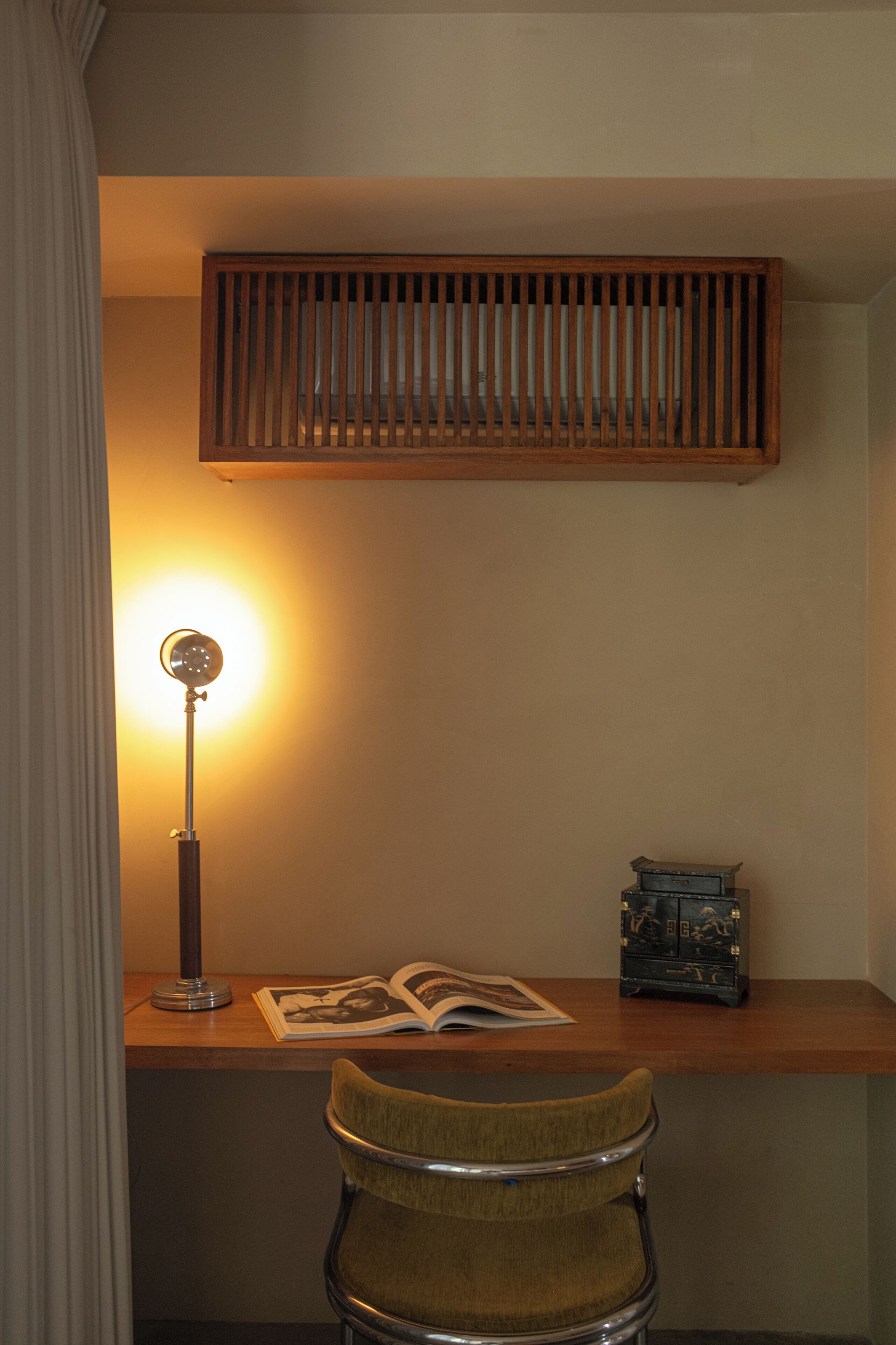 Um quarto com uma escrivaninha de madeira, uma lâmpada, uma cadeira e um pequeno baú decorativo.