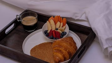 Un vassoio con un cornetto, una ciotola di frutta e una tazza di caffè su un letto.