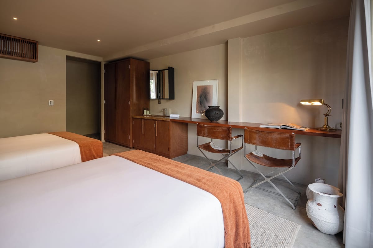 Une chambre d’hôtel avec deux lits, un bureau, une chaise, un miroir et une lampe.