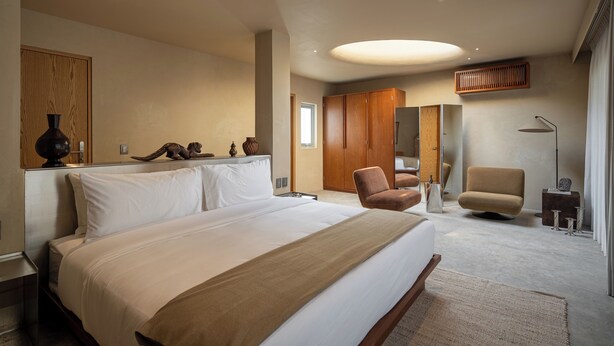 A modern bedroom with a large bed, wooden wardrobe, and two chairs.