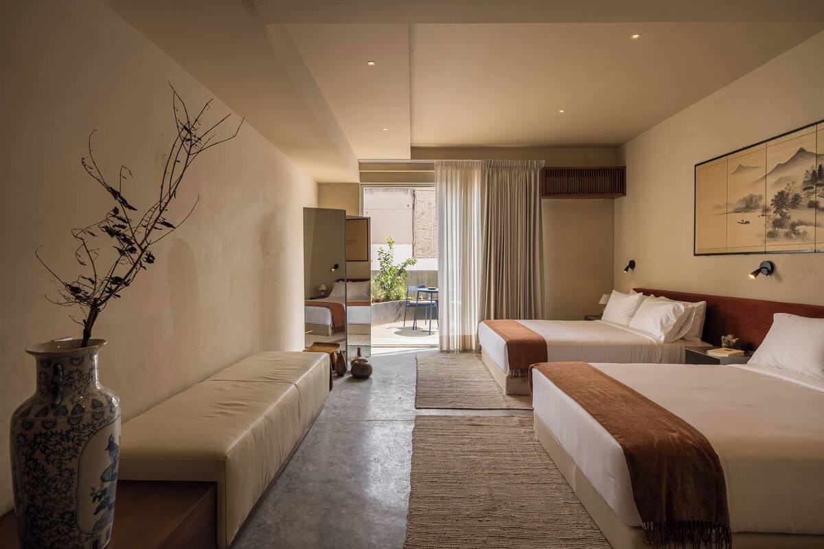 Une chambre d’hôtel avec deux lits, un canapé, un vase avec des branches et un tableau au mur.