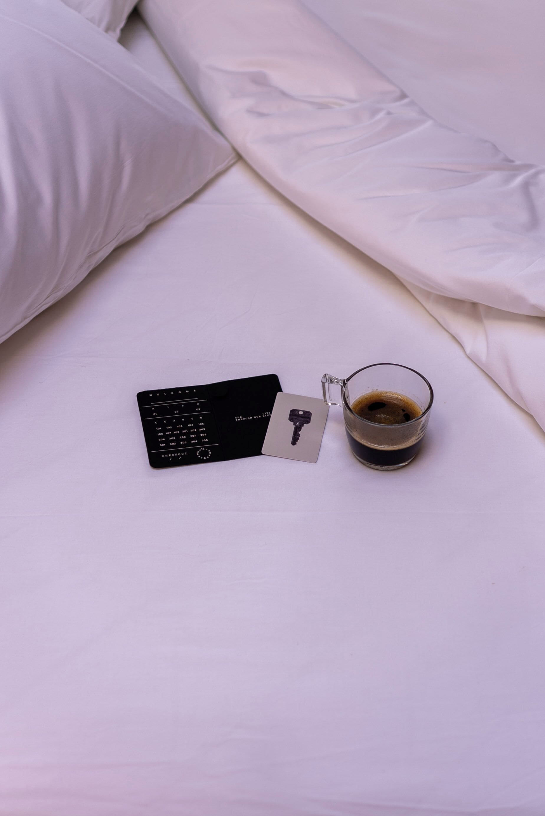 Un lit avec une literie blanche, une télécommande noire et une tasse de café posée sur le lit.