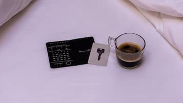 Un lit avec une literie blanche, une télécommande noire et une tasse de café posée sur le lit.