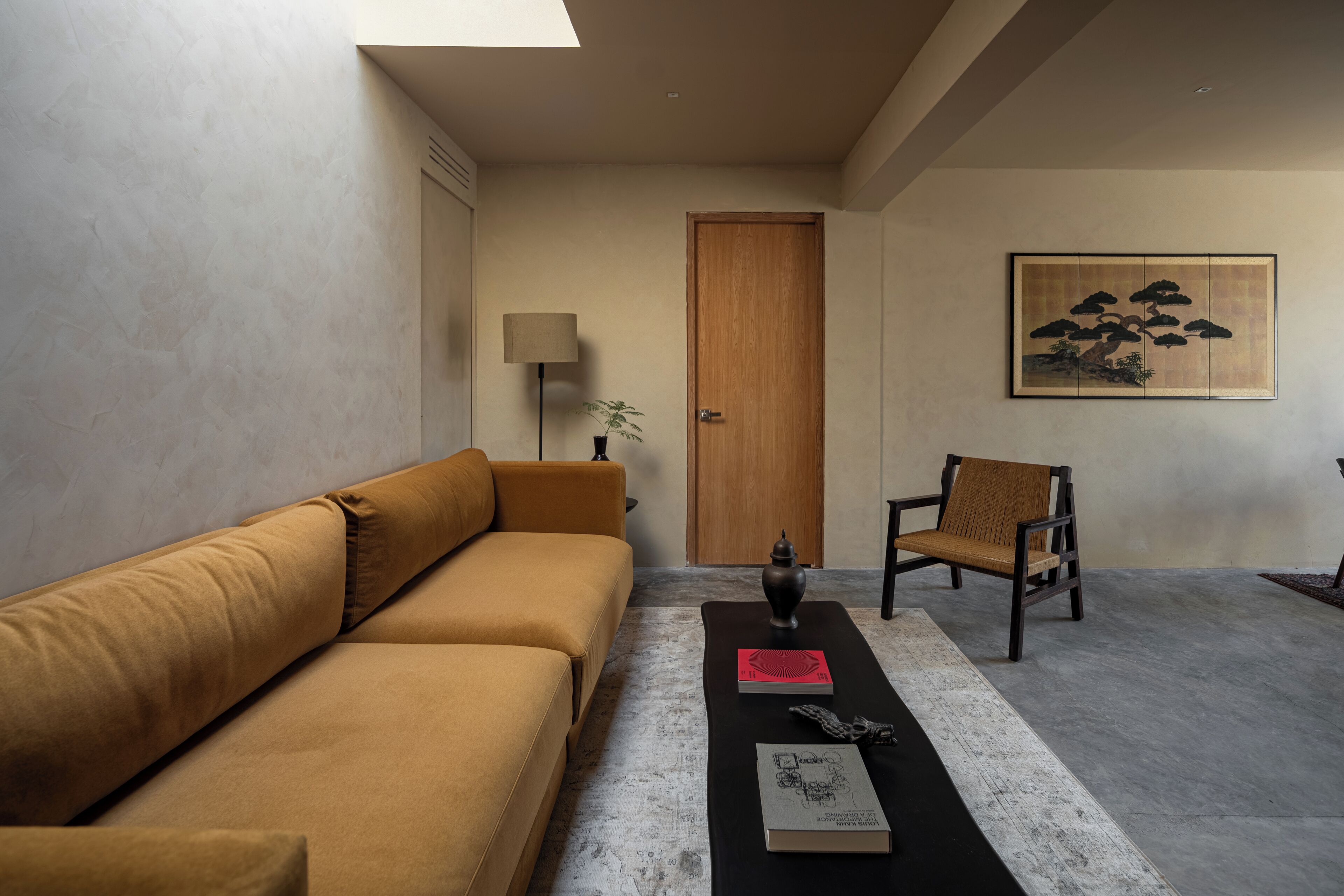 A modern living room with a sofa, a chair, a coffee table with books and a vase, a lamp, and a painting on the wall.