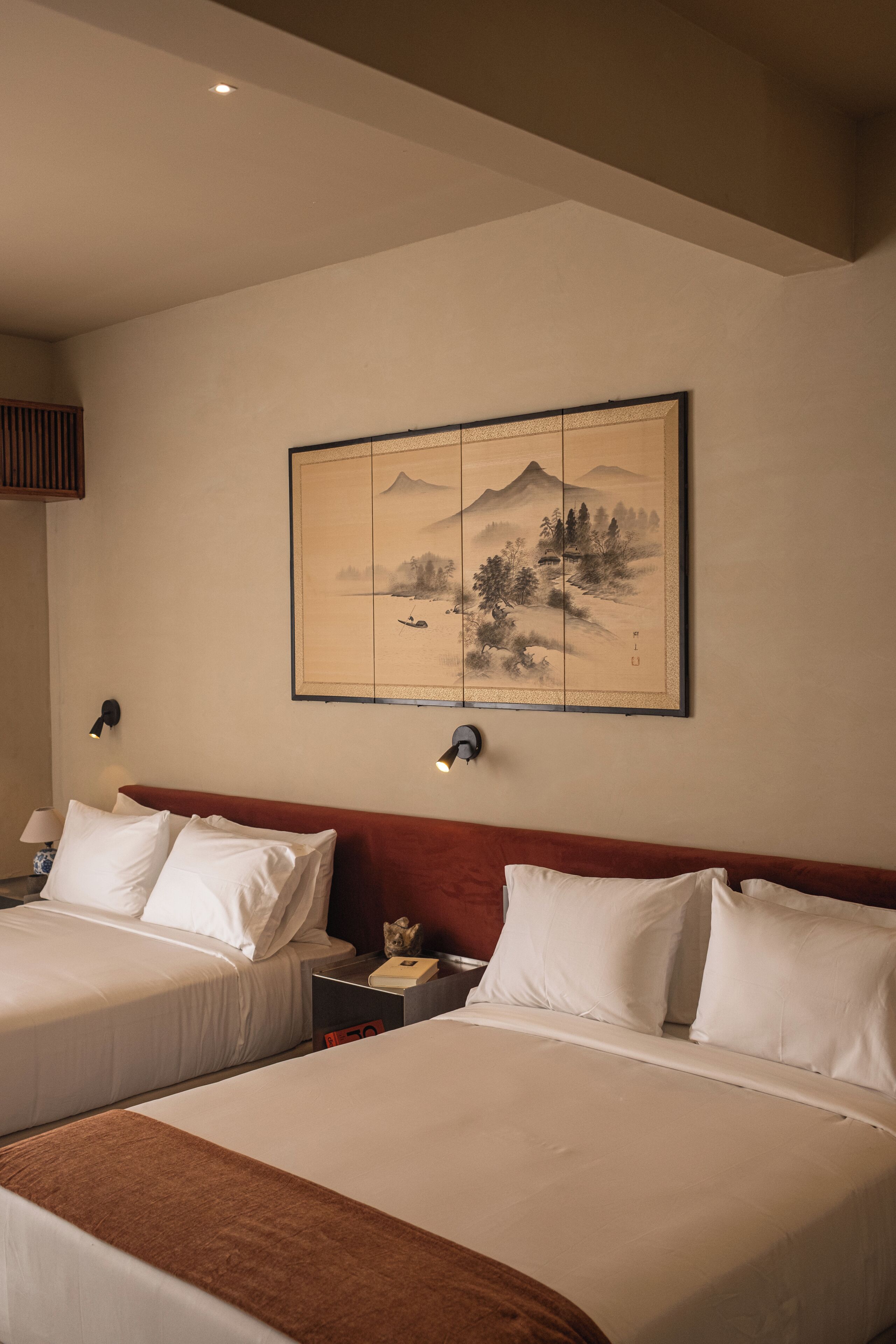 A hotel room with two beds, a large painting on the wall, and a nightstand with a lamp.