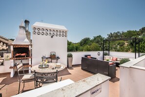 Um terraço no telhado com churrasqueira, área de estar e vista para o verde ao redor.