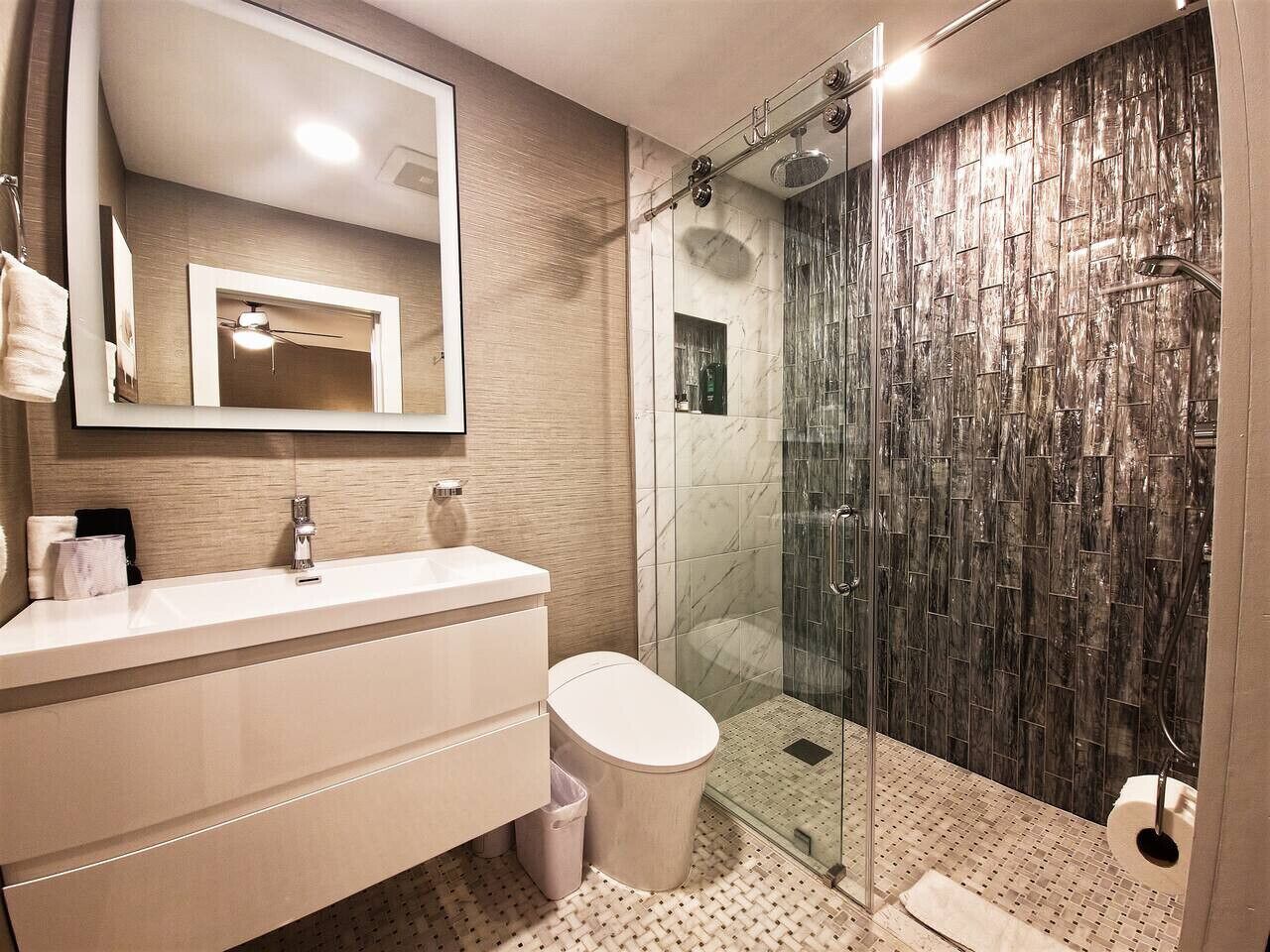Un baño moderno con ducha envuelta en vidrio, tocador blanco y un espejo grande.