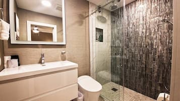 Un baño moderno con ducha envuelta en vidrio, tocador blanco y un espejo grande.