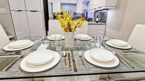 A modern dining area with a glass table set for four, surrounded by white chairs. A vase with yellow flowers is placed in the center. - Singer Island 3br/2ba Beach, Snorkel gear & Bikes (West Palm Beach)