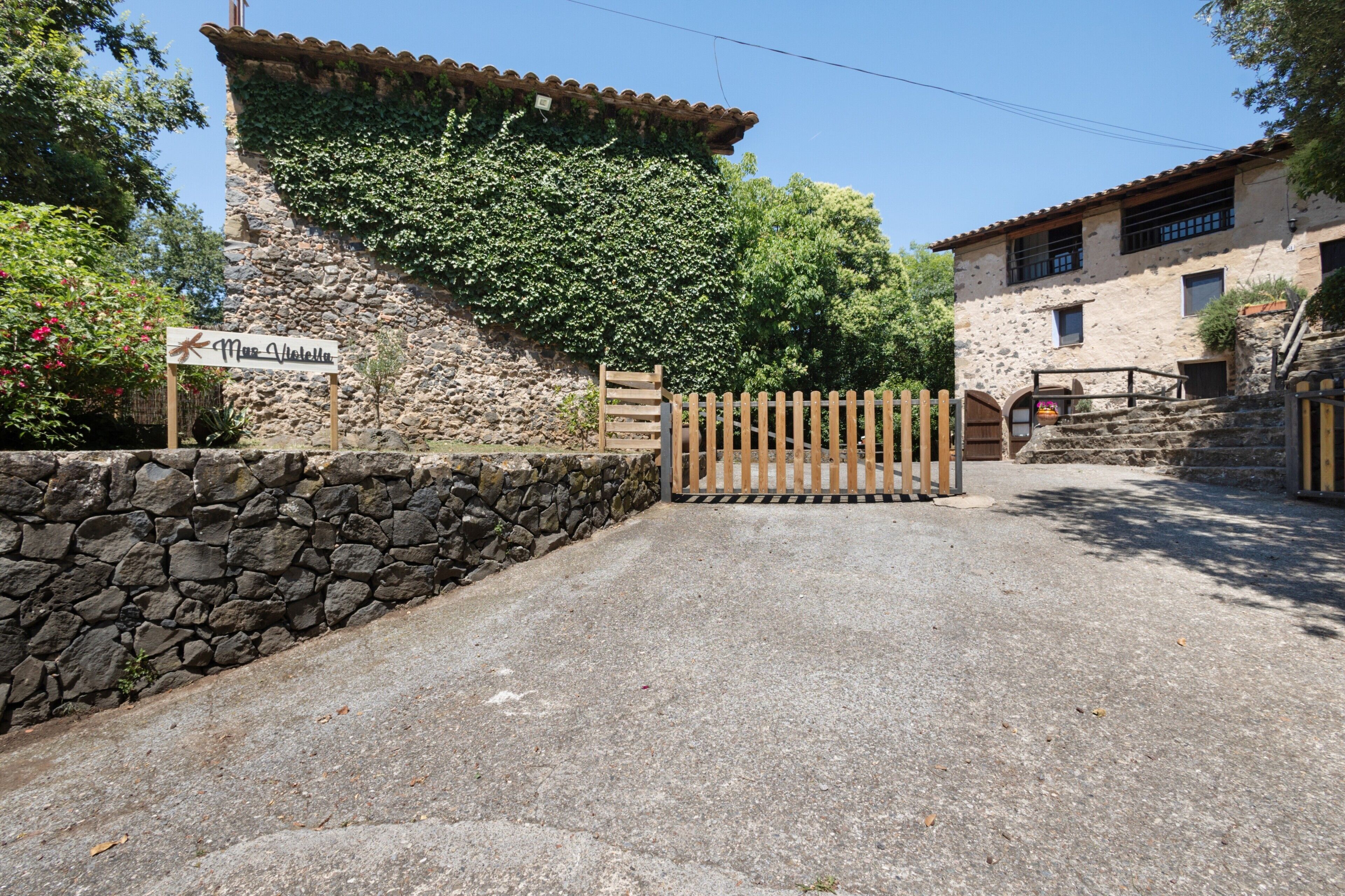 A stone wall with a sign, a wooden gate, and a building with a tiled roof.