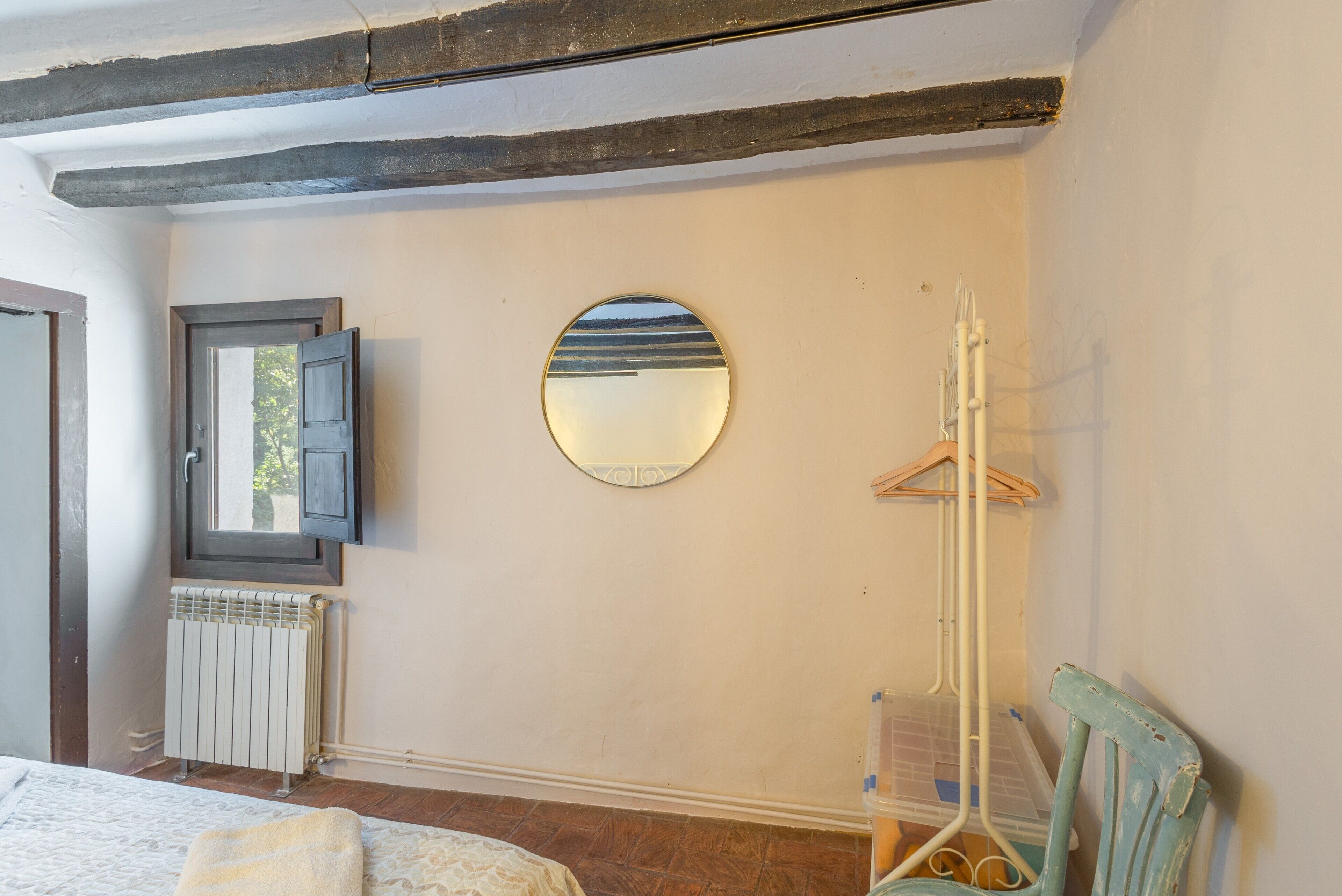 Une pièce comprenant un lit, un radiateur, un miroir, une chaise en bois et un porte-vêtements suspendu.