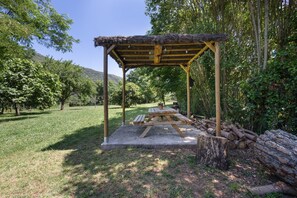A wooden gazebo with a thatched roof, a picnic table, and a stone bench.