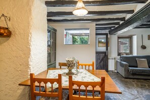 Un comedor con una mesa de madera, sillas, una lámpara colgante y vistas a través de una ventana.