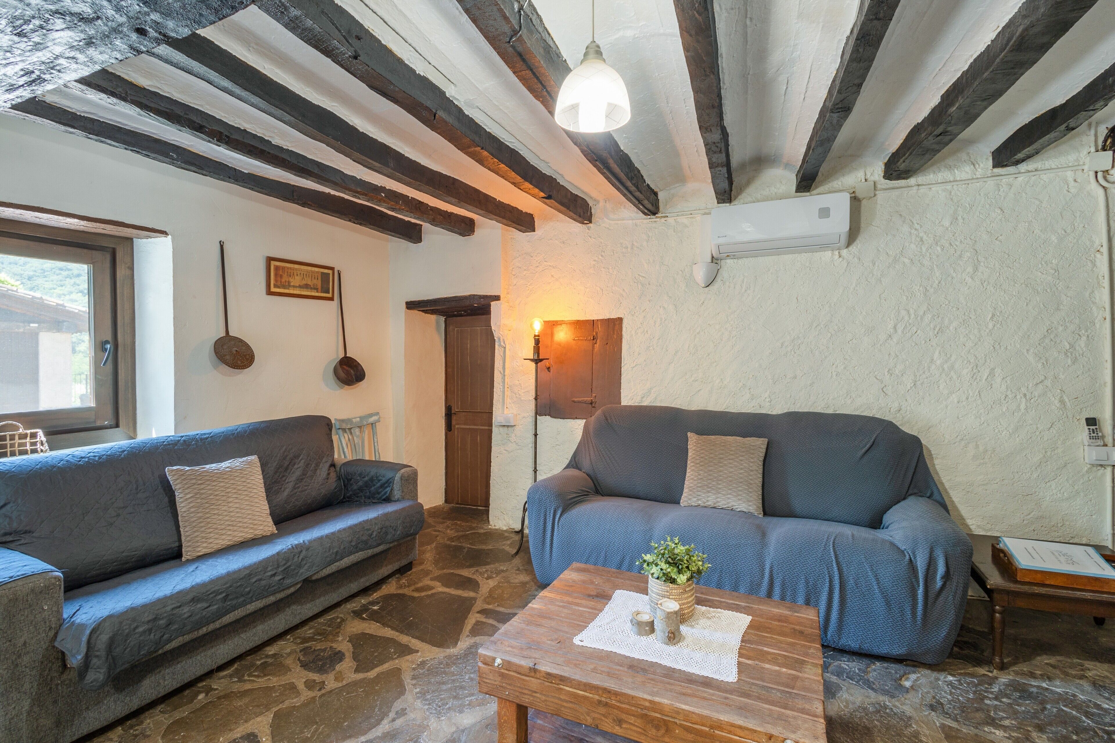 A room with stone flooring, two sofas, a wooden coffee table, a hanging light fixture, and a door.