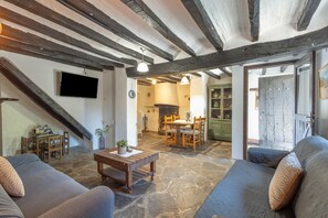 A rustic interior with exposed beams, stone flooring, a wooden table, and a sofa. - Cargol de Mas Violella: rural charm in natural park, direct garden access, pool & wifi (Sant Joan Les Fonts)