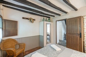 Una habitación con una cama, una silla de mimbre, un armario y un espejo.