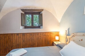 Ein Schlafzimmer mit Holz-Kopfteil, einem Einzelbett mit Quiltdecke, einem Nachttisch mit Lampe und einem Fenster mit Blick auf Bäume.