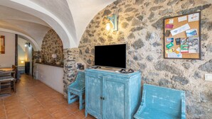 Un interior rústico con paredes de piedra, un televisor sobre un mueble y un tablón de corcho con diversas notas.