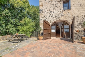 Ein rustikales Steinhaus mit offener Holztür, die in einen Raum mit einem Bett und Vorhängen führt.