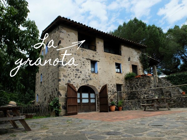 A rustic stone building with a tiled roof, wooden doors, and a stone staircase leading to the entrance.