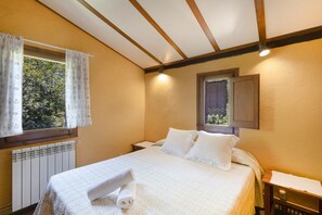 A bedroom with a bed, a window with curtains, a radiator, and a small bedside table.