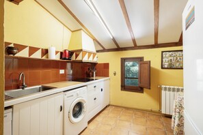 A kitchen with a washing machine, a sink, and a window with a view of greenery.