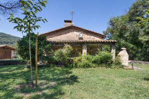 A stone house with a tiled roof, surrounded by a grassy yard and trees.