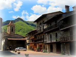 A traditional stone building with a bell tower, a car parked in front, and a mountainous backdrop. - Granota de Mas Violella Country House: Natural Park, Views, Pool & Wi-Fi (Sant Joan les Fonts)