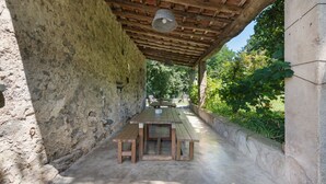 Patio esterno con parete in pietra rustica, panche in legno e struttura del soffitto in legno.