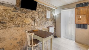 Una stanza con parete in pietra, un tavolo in legno, una sedia, un televisore a parete e una porta con tenda.