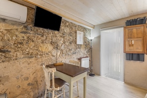 Ein Zimmer mit Steinwand, einem Holztisch, einem Stuhl, einem an der Wand montierten Fernseher und einer Tür mit Vorhang.