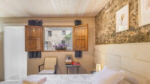 Una camera da letto con un letto, una sedia, un tavolino e una finestra con persiane aperte.