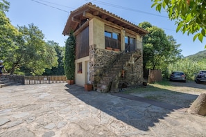 A stone house with a wooden balcony, a paved driveway, and parked cars in the background. - Cabana at Mas Violella: Charm, Views, and Natural Light. Air Conditioning & Wi-Fi (Sant Joan les Fonts)