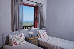 A bedroom with two beds, a window with curtains, a bedside table with a lamp, and a view of the landscape. - Amorosa Villas (Zakynthos)