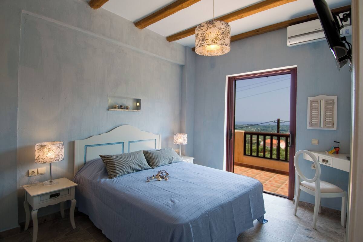 A bedroom with a bed, bedside lamps, a desk, and a balcony with a view.