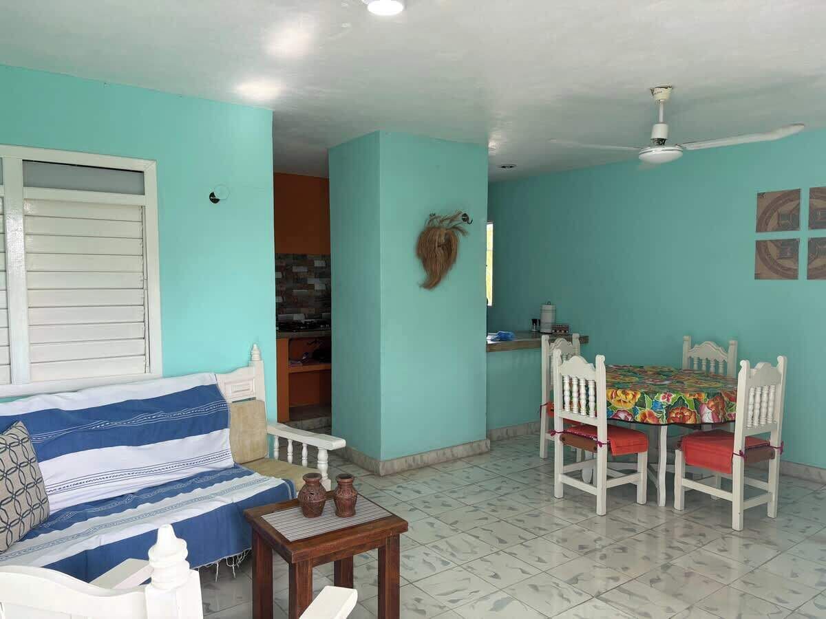 A room with a blue wall, a white ceiling fan, a dining table with chairs, a sofa, and a small table with decorative items.