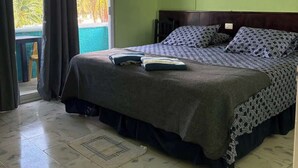 A hotel room with a bed, a ceiling fan, a nightstand, a wall-mounted lamp, and a view of a pool through a sliding door. - Delightful Beach Time in Chelem! (Chelem)