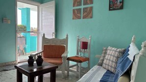 A room with a teal wall, a white bed with patterned pillows, a wooden chair, a small table with two vases, and a painting on the wall. - Delightful Beach Time in Chelem! (Chelem)