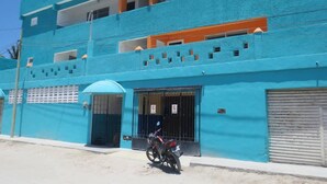 Um edifício de dois andares com fachada azul, uma motocicleta estacionada em frente e uma entrada com portão.