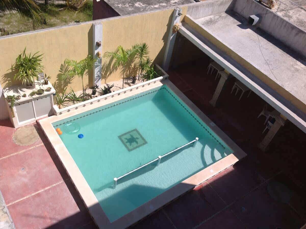 A rectangular pool with a safety sign, surrounded by potted plants and a tiled deck.