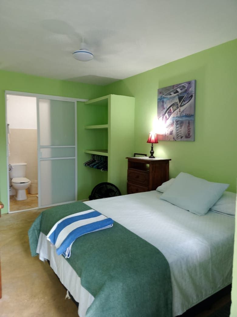 A bedroom with a bed, a nightstand, a lamp, a painting on the wall, and a closet with hanging clothes.