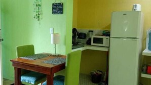 Cozinha compacta com geladeira, micro-ondas e fogão. Há uma mesa de jantar com cadeiras e um tapete pequeno.