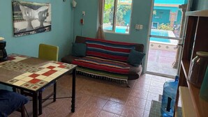 Ein Zimmer mit einer Couch, einem Tisch mit einer Tagesdecke, einem großen Wasserspender und Blick auf einen Pool durch eine Glastür.
