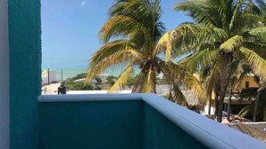A balcony with a view of palm trees and a building in the background. - Comfortable Beach Living in a Mexican village! (Chelem)